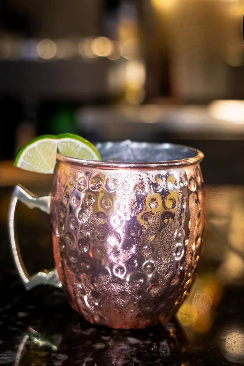 A cold Moscow Mule in a hammered copper mug, garnished with a fresh lime wedge.