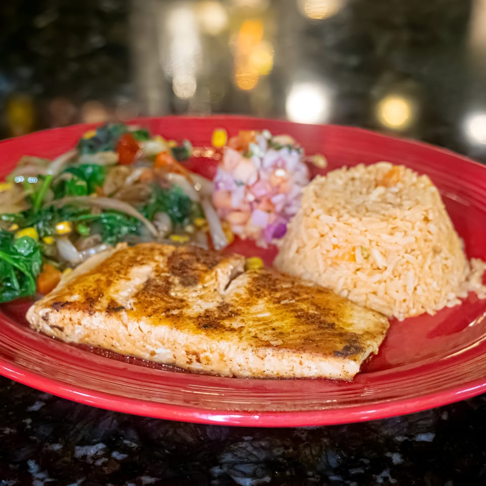 Grilled fish with rice, mixed vegetables, and pico de gallo on a red plate.