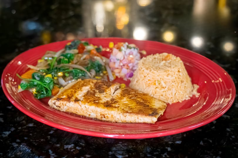 Grilled fish with rice, mixed vegetables, and pico de gallo on a red plate.