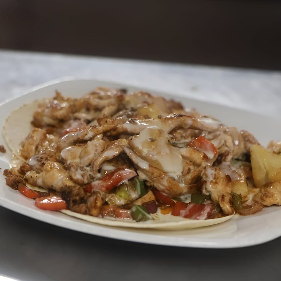 Chicken fajitas with peppers, onions, and a creamy sauce on a tortilla, served on a white plate.