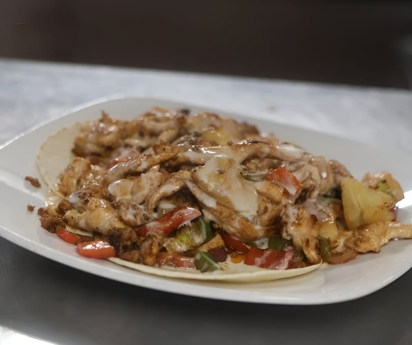 Chicken fajitas with peppers, onions, and a creamy sauce on a tortilla, served on a white plate.