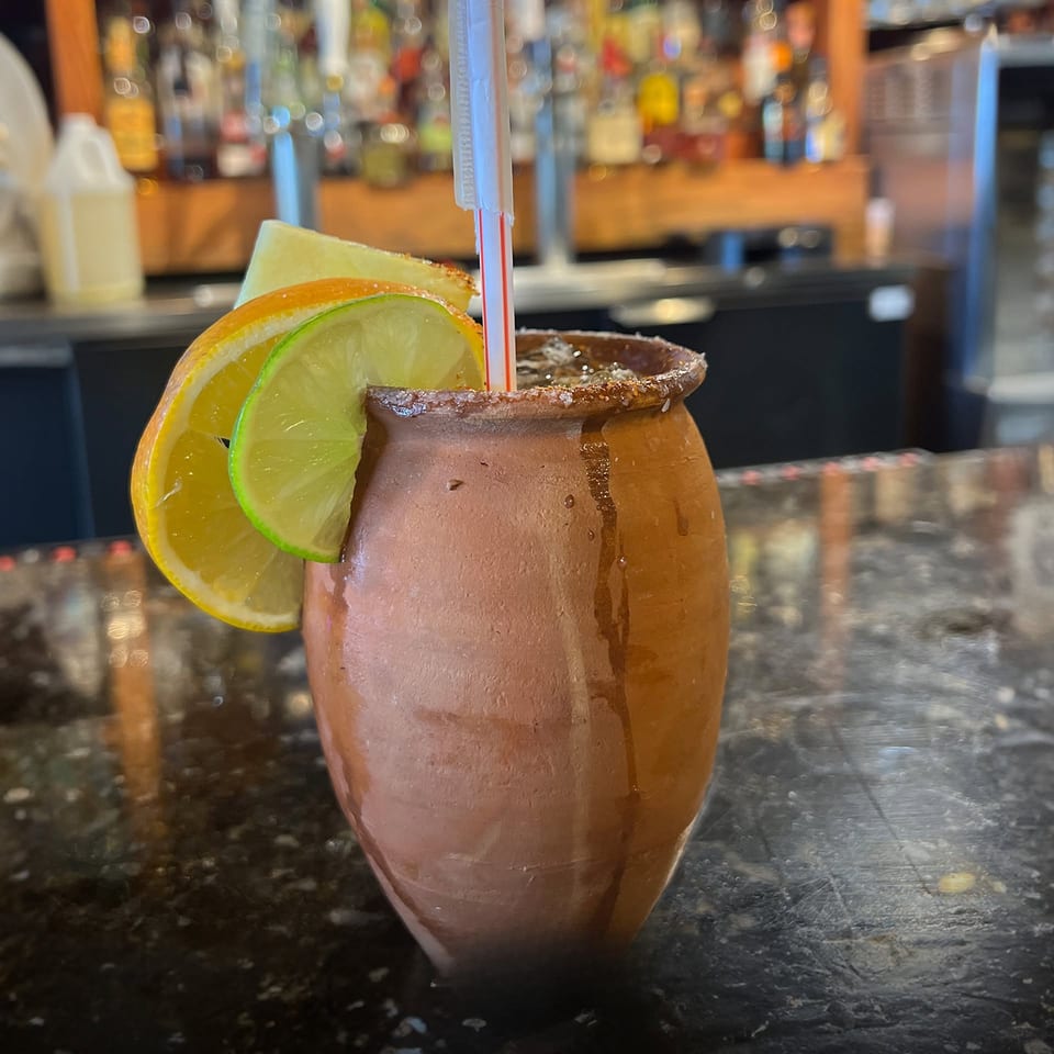 A clay mug with a drink, garnished with orange, lime, and pineapple slices, on a bar.